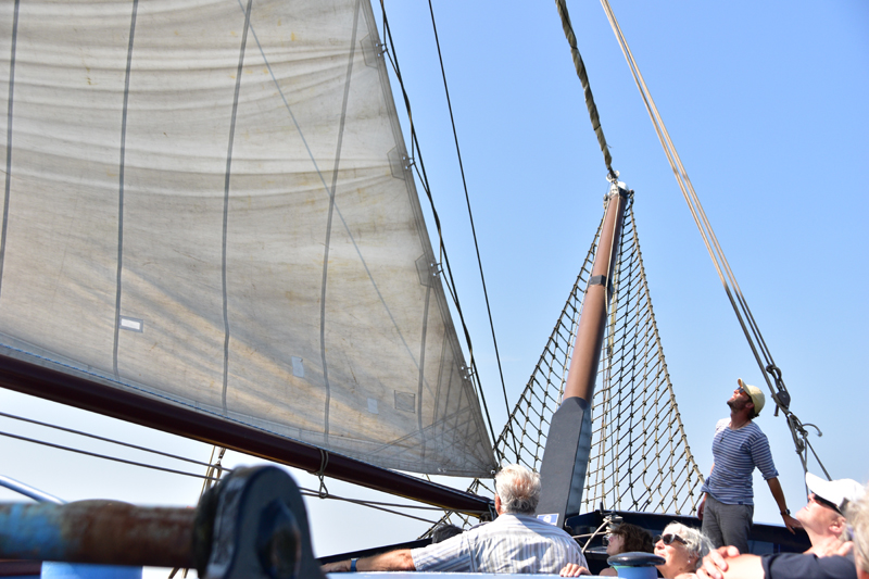 The skipper on the Mare fan Fryslan hoists the sails and explains some features to the passengers.