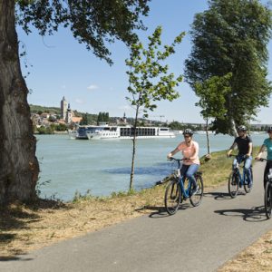 Three people cycling next to the water.